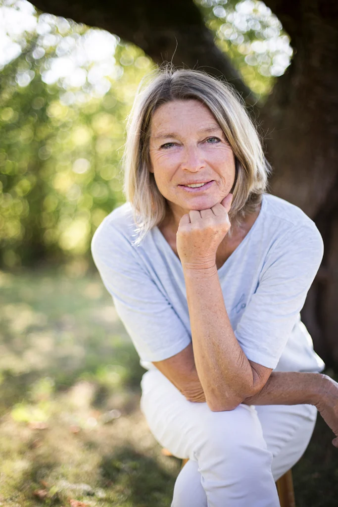 Maren Jans, Heilpraktikerin, sitzt im Garten unter einem Baum und stützt das Kinn auf die Hand